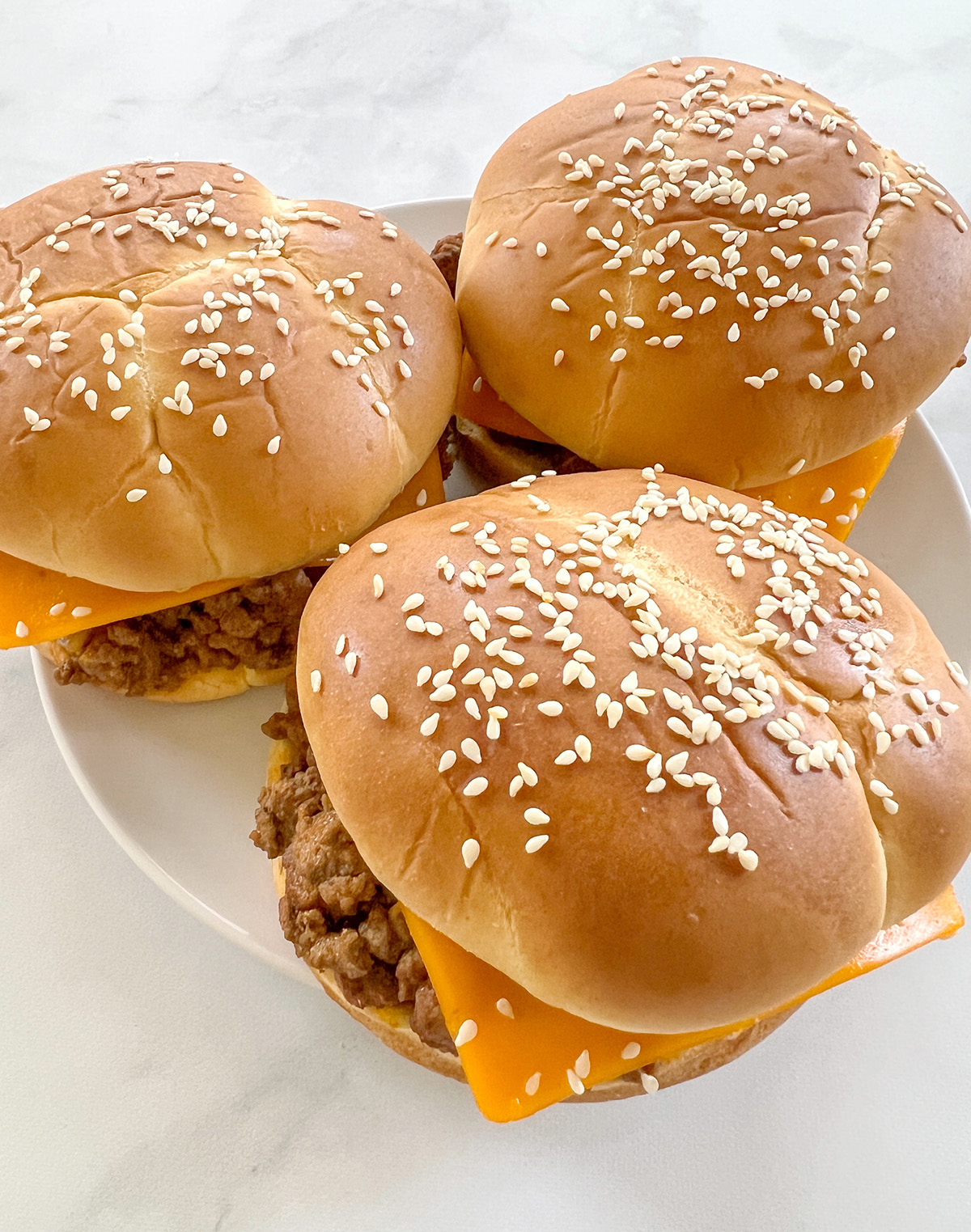 This is a photo of 3 ground beef sliders served on a white plate. 