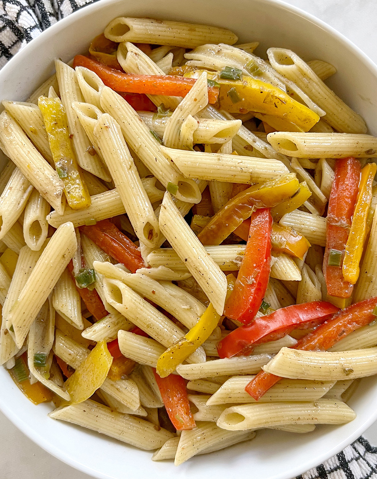 vegan rasta pasta with bell peppers and green onion in a white bowl.