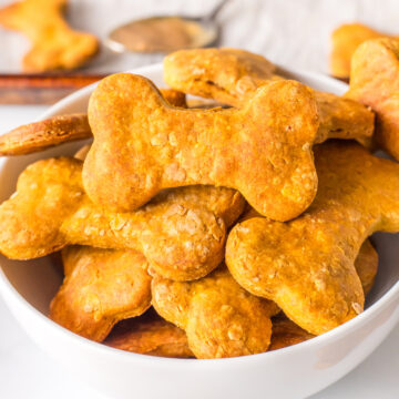 Bowl of homemade pumpkin peanut butter dog treats stacked in bone shapes