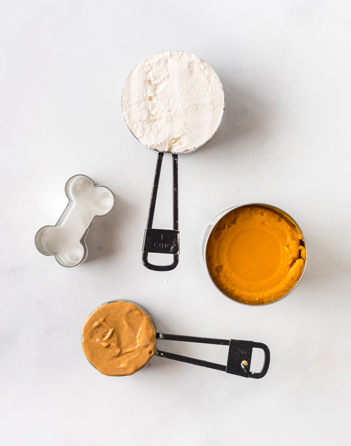 Measured ingredients for homemade dog treats, flour, pumpkin, and peanut butter