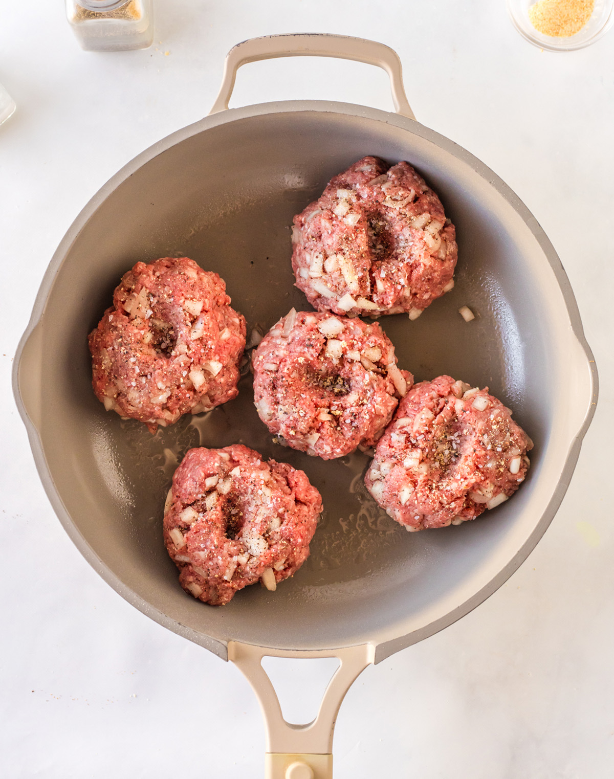 uncooked burger patties cooking in a skillet before flipping