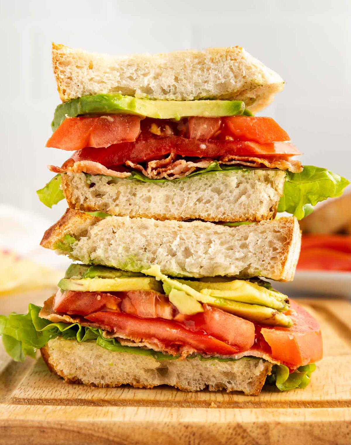 Stacked BLTA halves showing bacon, lettuce, tomato, and avocado