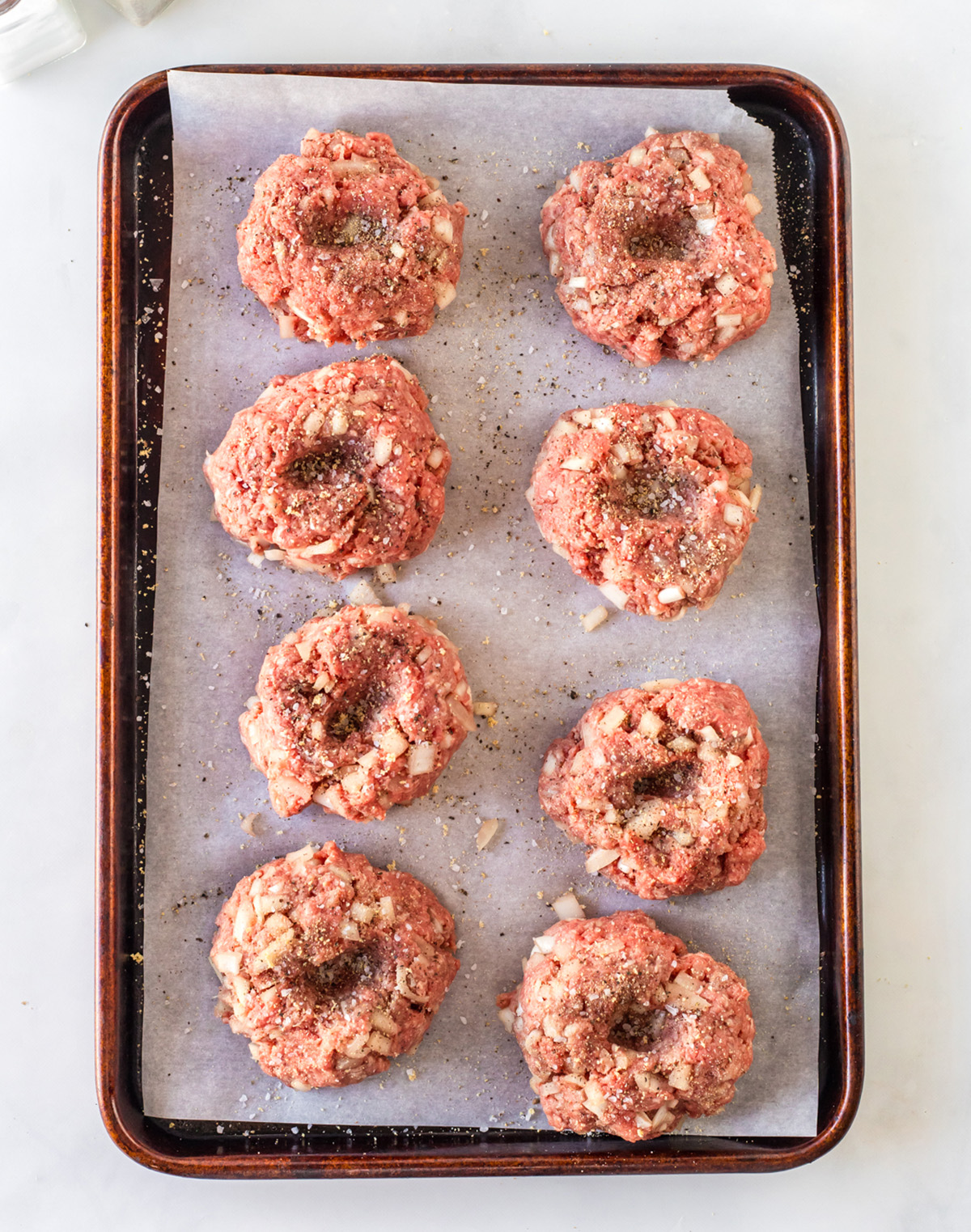 Uncooked burger patties with thumb dents on a baking sheet