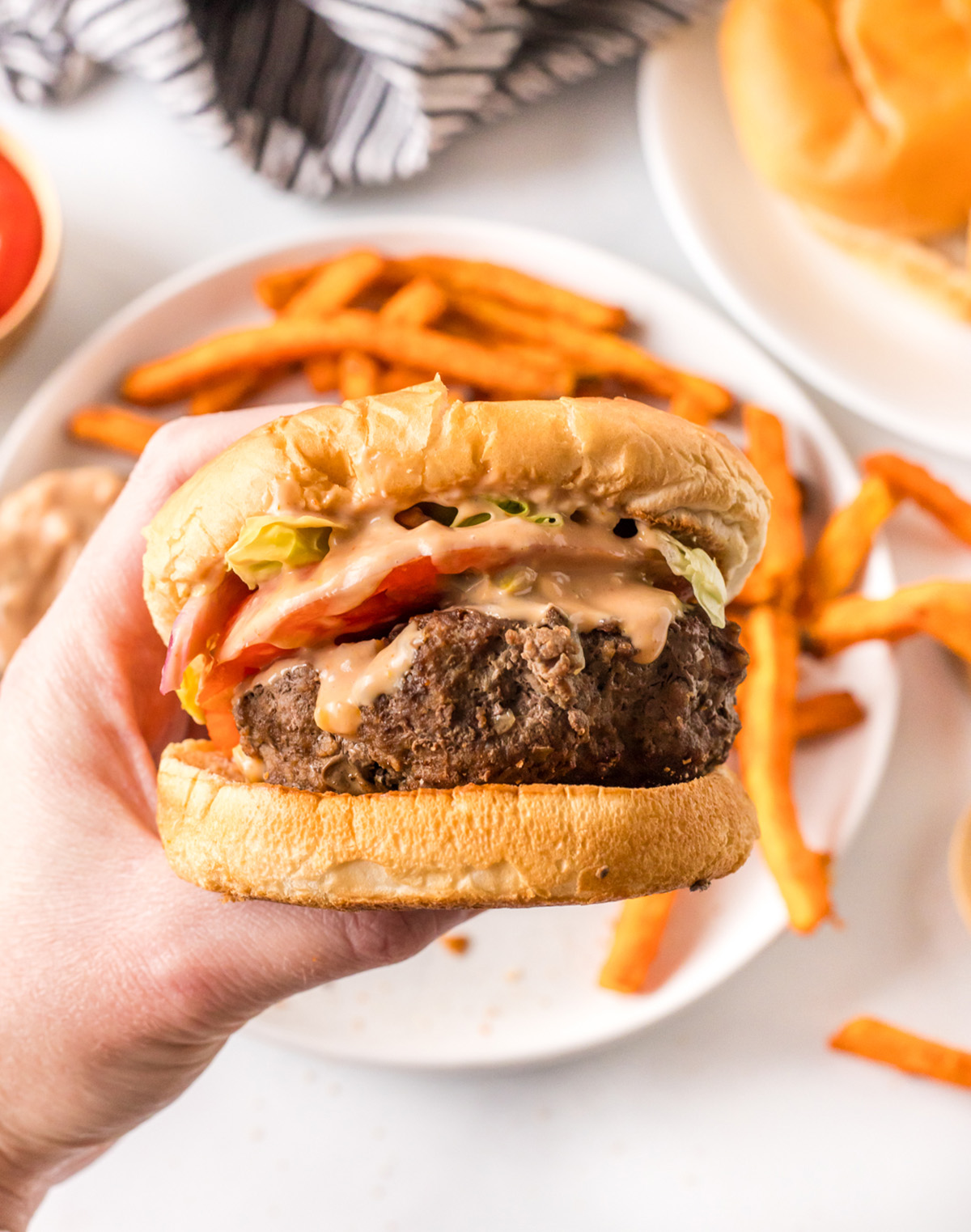hand holding a dairy free burger dipped in burger sauce