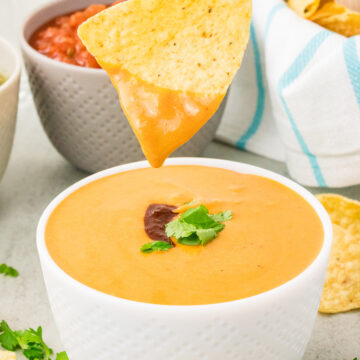 spicy vegan nut free queso cheese sauce with tortilla chip dipping