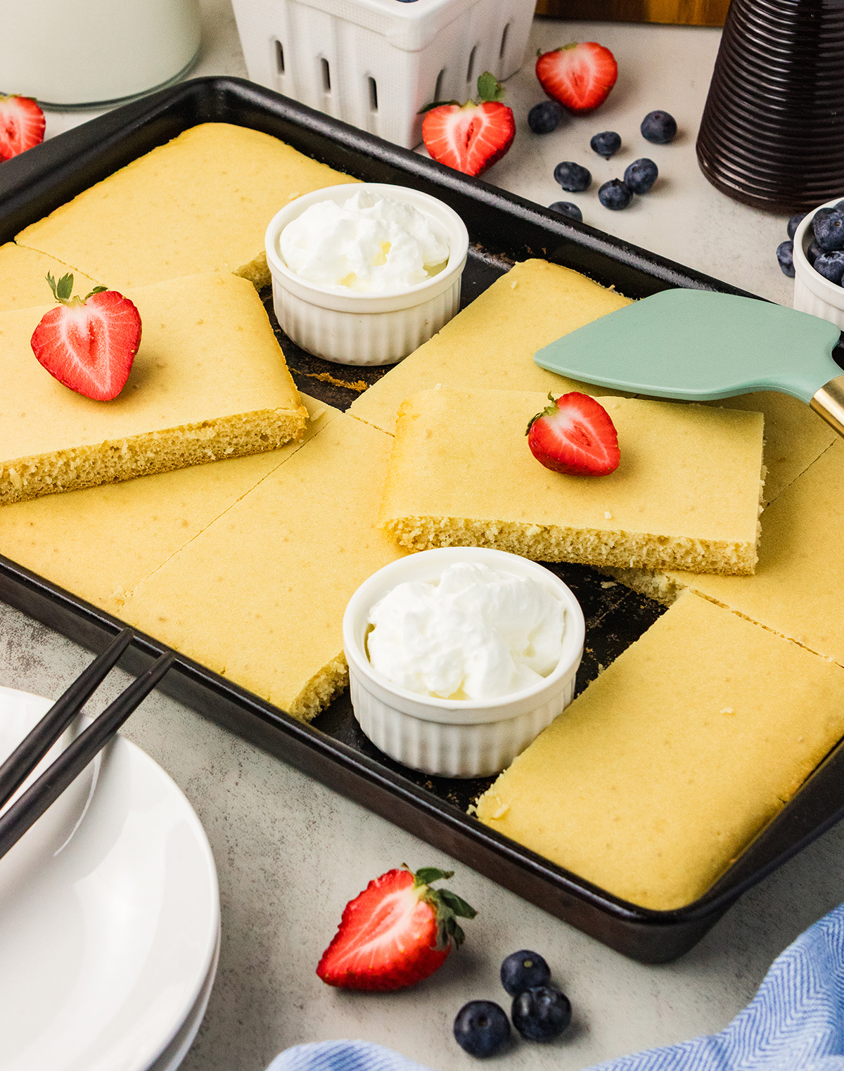 Dairy free and egg free sheet pan pancakes cut into squares with a few pieces pulled out, served with vegan whipped topping and berries.