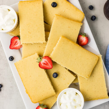 Platter of easy dairy-free sheet pan pancakes cut into rectangles, with vegan whipped topping and fresh berries.