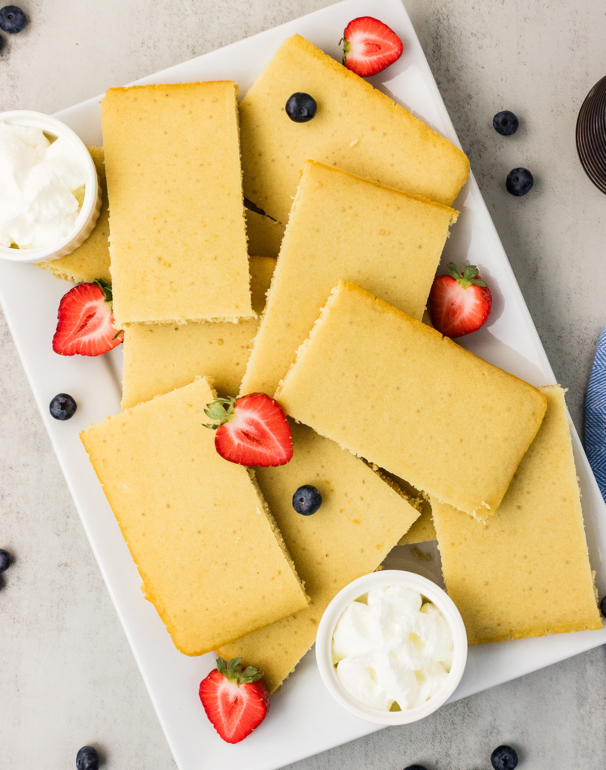 Platter of easy dairy-free sheet pan pancakes cut into rectangles, with vegan whipped topping and fresh berries.