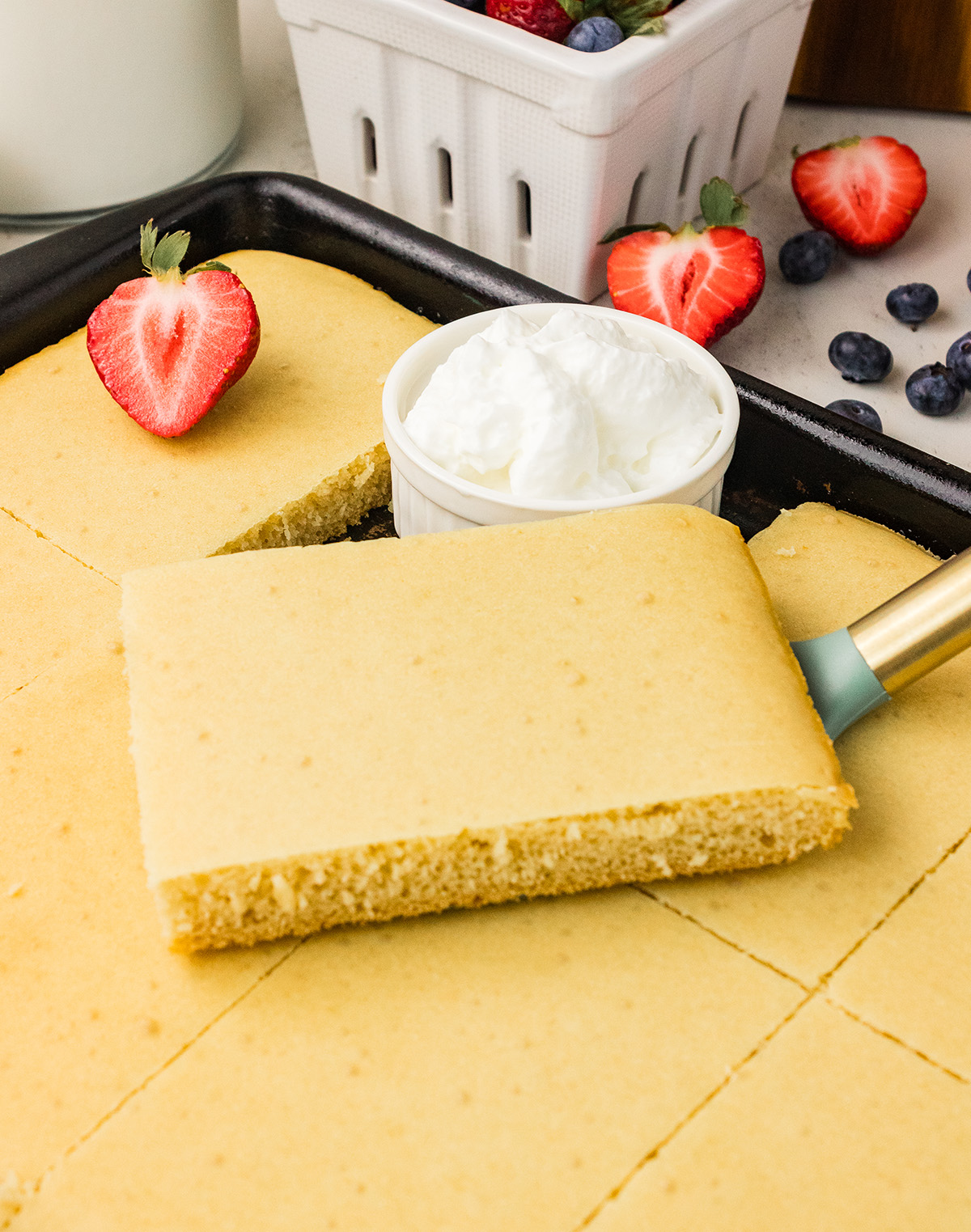 Spatula lifting a square of eggless sheet pan pancake to show the soft, airy crumb inside.