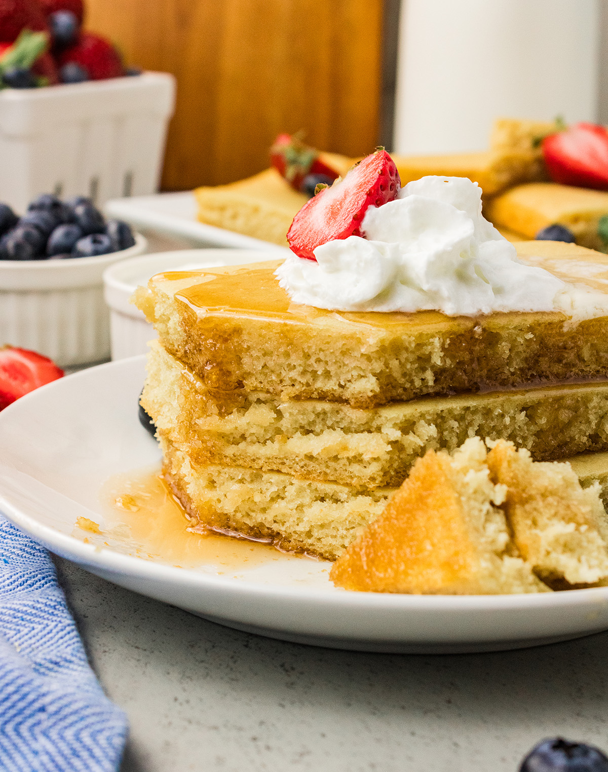 Stack of three vegan sheet pan pancakes with whipped topping, syrup and a strawberry, with a bite on a fork.