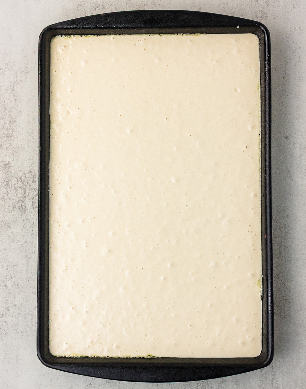 Vegan pancake batter poured evenly into a black sheet pan, ready to bake in the oven.